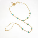 A gold chain anklet featuring seven small round turquoise blue gemstones set in gold bezels, displayed on a clean white background.