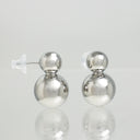 A pair of silver double-ball stud earrings with clear silicone ear wires, displayed on a reflective light gray surface.