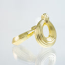 A polished gold ring with a textured, ribbed spiral design, displayed on a reflective white surface against a light gray background.