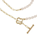 Gold chain necklace with a four-leaf clover charm, paperclip links, and a toggle clasp, paired with a strand of white baroque pearls on a white background.