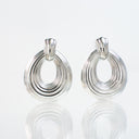 A pair of silver-toned hoop earrings with a textured, ribbed circular design and a small top loop, displayed on a reflective white surface against a white background.