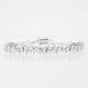 A silver tennis bracelet featuring marquise-cut and baguette diamonds, displayed on a clean white reflective surface.