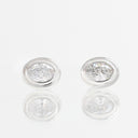 A pair of oval stud earrings with clear gemstones in a silver-toned bezel setting, displayed on a reflective white surface.