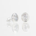 A pair of oval stud earrings with clear gemstones in polished silver settings, displayed on a reflective white surface.