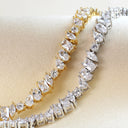 Two tennis-style bracelets displayed on a cream satin surface, one in yellow gold and one in silver-tone metal, both set with clear pear-cut gemstones.