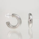A pair of silver crescent-shaped hoop earrings with a ribbed, textured exterior and clear butterfly backings, displayed on a reflective light gray surface.