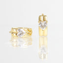 A pair of gold heart-shaped ring earrings with clear heart-cut gemstones, shown from both front and side angles on a reflective white surface.