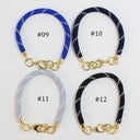 Four elastic wristlets with gold-tone clasp hardware arranged in a 2x2 grid on a white background. Each wristlet has a different colorway: blue with white diagonal stripes (#09), navy with white diagonal stripes (#10), light gray with white diagonal stripes (#11), and black with white diagonal stripes (#12).