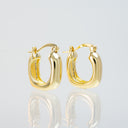 A pair of polished gold hoop earrings with a thick, rounded double-hoop design, displayed on a reflective light gray surface.