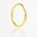 A classic yellow gold band ring with a smooth, polished finish, standing upright on a reflective white surface against a white background.