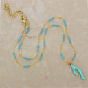 A gold-tone beaded necklace with small turquoise blue beads and a light turquoise pendant, displayed on a beige marble surface.