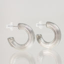 A pair of silver crescent-shaped hoop earrings with a textured, ridged outer surface and clear butterfly backings, displayed on a reflective light gray surface.