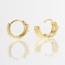 A pair of gold huggie hoop earrings with a small clear gemstone, displayed on a reflective white surface against a white background.