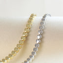 Two heart-link bracelets, one gold-toned and one silver-toned, displayed on a cream fabric surface.