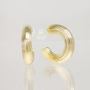 A pair of gold hoop earrings with a textured, ridged concentric design, shown on a reflective light gray surface.