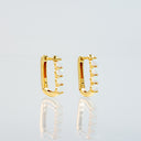 A pair of gold huggie hoop earrings with a row of white opal gemstones, displayed on a reflective light gray surface.