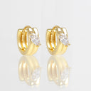 A pair of gold huggie hoop earrings, each featuring a marquise-cut clear gemstone in a prong setting, displayed on a reflective white surface.