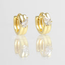 A pair of gold huggie hoop earrings with a pear-cut clear gemstone in the center of each earring, displayed on a reflective white surface.