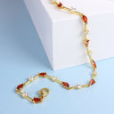 A gold-plated tennis bracelet with marquise-cut amber-red crystals and small clear cubic zirconia accents, displayed on a light blue surface next to a white block.