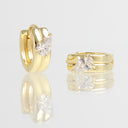 A pair of gold hoop earrings with pear-cut clear gemstones, shown standing upright and lying flat on a reflective light gray surface. The gemstones are clear and do not contribute to the color classification, leaving the yellow gold metal as the sole product color.