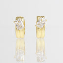 A pair of gold huggie hoop earrings with rectangular clear gemstones, displayed on a reflective white surface against a light gray background.