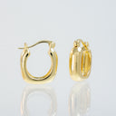 A pair of polished yellow gold hoop earrings shown on a light gray reflective studio background, with one earring facing forward and the other angled to show the side and back.