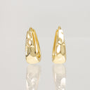A pair of gold hoop earrings with a textured, hammered surface, displayed on a reflective light gray surface.