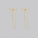 A pair of gold bow-shaped dangle earrings with a small oval pearl center and long dangling chains, shown on a solid gray background.