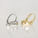 Two textured hoop earrings on a reflective white surface, one in polished silver and one in polished yellow gold.