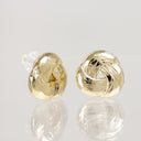 A pair of gold knot stud earrings with a polished, reflective finish, displayed on a light gray reflective surface.