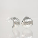 A pair of textured silver stud earrings with a hammered, ribbed surface, displayed on a reflective white surface against a light gray background.
