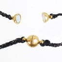 Black braided cord bracelets with polished gold-tone metal accents, including a central round gold bead and two smaller gold dome-shaped beads with circular silver-toned inlays, shown on a white background.