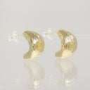 A pair of gold crescent-shaped hoop earrings with a textured, ribbed surface, shown on a reflective light gray surface.