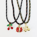 Three fashion necklaces with black cords and gold-tone charms, featuring red cherry, red ladybug, and gold cherub pendant designs on a white background.
