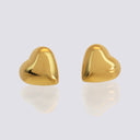 A pair of shiny gold heart-shaped stud earrings on a light gray reflective surface.