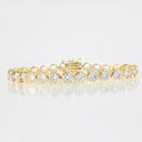 A yellow gold tennis bracelet featuring round-cut clear gemstones in bezel settings, displayed on a reflective white surface against a light gray background.