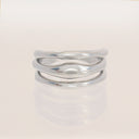 A polished silver wavy ring with three interlocking curved bands, displayed on a clean white reflective surface.
