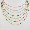 A set of six layered beaded necklaces with gold-tone chains and colorful beads, displayed on a plain light gray background.
