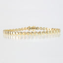 A yellow gold tennis bracelet with flat, circular disc-shaped links, displayed on a clean white reflective surface.