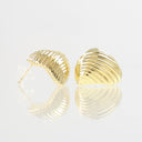 A pair of gold-toned, ribbed clamshell stud earrings on a reflective white surface.