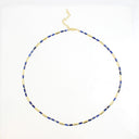 A delicate gold chain necklace featuring alternating segments of polished gold tubes and small rectangular blue gemstones, displayed on a clean white background.