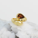 A gold ring with a teardrop-shaped amber gemstone, displayed on a white crystal cluster against a light gray background.
