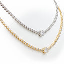 Two tennis-style necklaces with round clear stones, shown on a white background. One necklace is silver-toned and the other is yellow gold-toned, each featuring a larger central round stone.