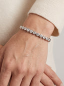A close-up of a person's wrist wearing a silver tennis bracelet with round clear stones, paired with a cream-colored knit sweater.