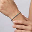 A close-up of a delicate bracelet worn on a person's wrist, featuring small round turquoise-blue stones set in a gold-toned band, with fingers gently resting near the wrist against a soft light gray background.