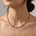 A close-up of a model wearing a delicate necklace made of alternating deep blue and gold cylindrical beads.