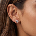A close-up of a woman's ear wearing a small oval stud earring with a silver-toned bezel and clear gemstone.