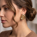 A close-up side profile of a woman wearing a large, polished gold spiral drop earring.