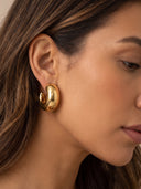A close-up side profile of a woman wearing a polished gold spiral-shaped hoop earring.