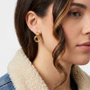 A close-up of a woman wearing a gold hoop earring with three stacked circular rings, styled with a denim jacket featuring a cream sherpa collar.